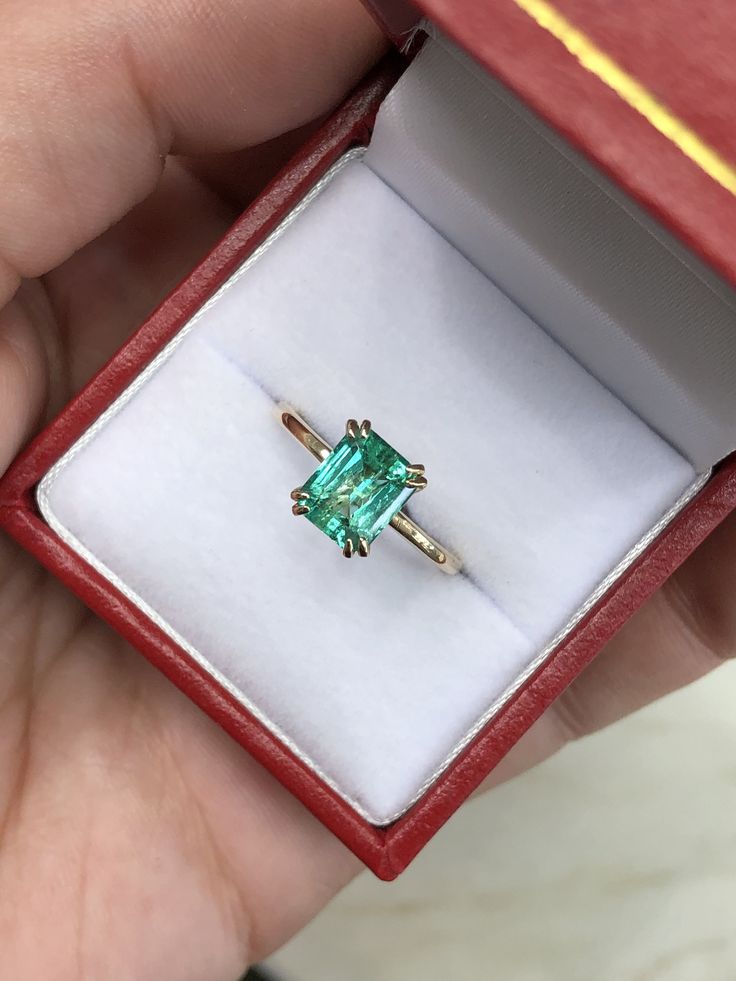 someone is holding an emerald ring in a red box with gold trimmings on it