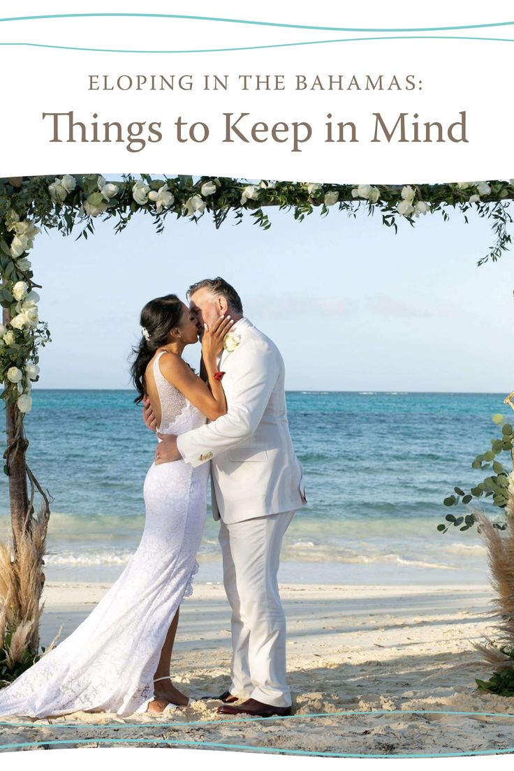 a bride and groom kissing under an arch on the beach