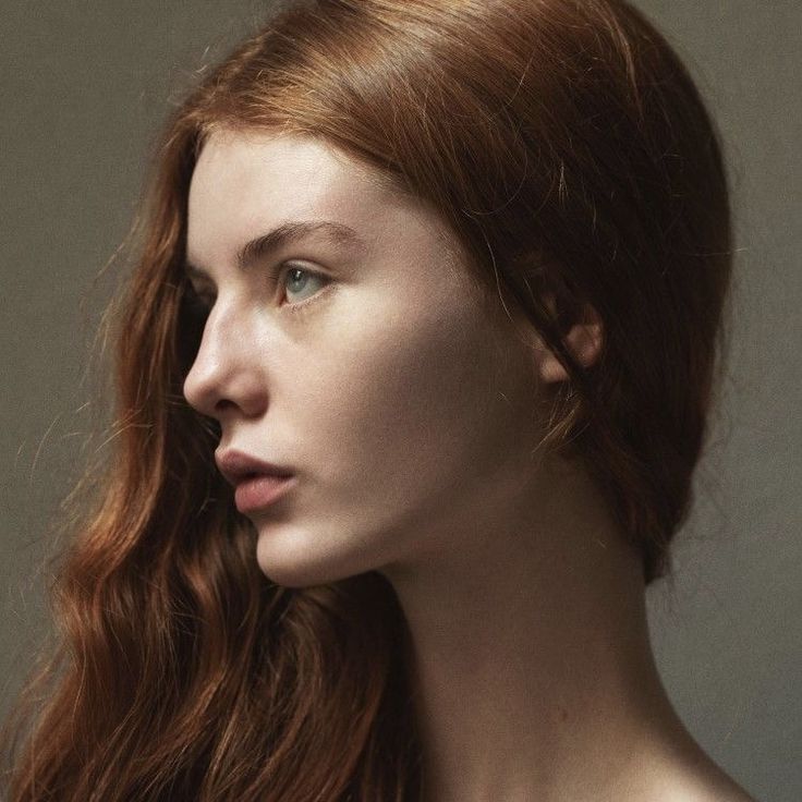 a woman with long red hair is looking off to the side and has blue eyes