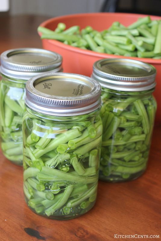 three jars filled with green beans sitting on top of a wooden table