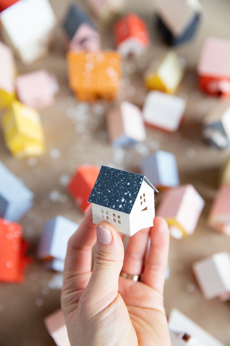 a hand holding a tiny house in front of many smaller houses on the ground,