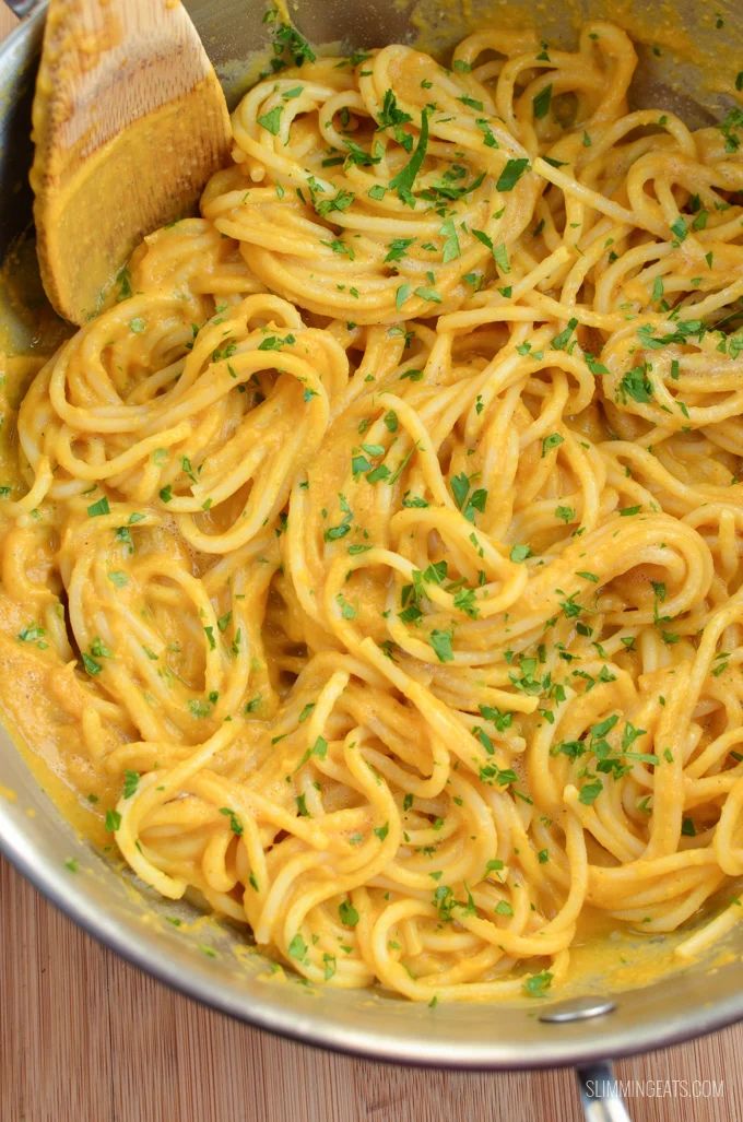 a pan filled with pasta and parsley on top of a wooden table