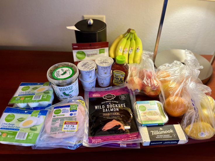 Groceries sitting on a table inside a hotel. Healthy Hotel Eating, Meals To Make In A Hotel Room, Easy Meals For Hotel Stays, Stocked Mini Fridge Snacks, Hotel Meals No Microwave, Meal Prep For Hotel Stay, Healthy Hotel Snacks, Healthy Hotel Room Meals, Hotel Meal Prep