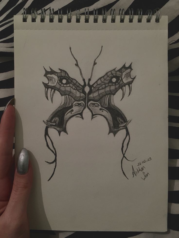 a hand holding a pencil drawing of a butterfly on a piece of paper with black ink