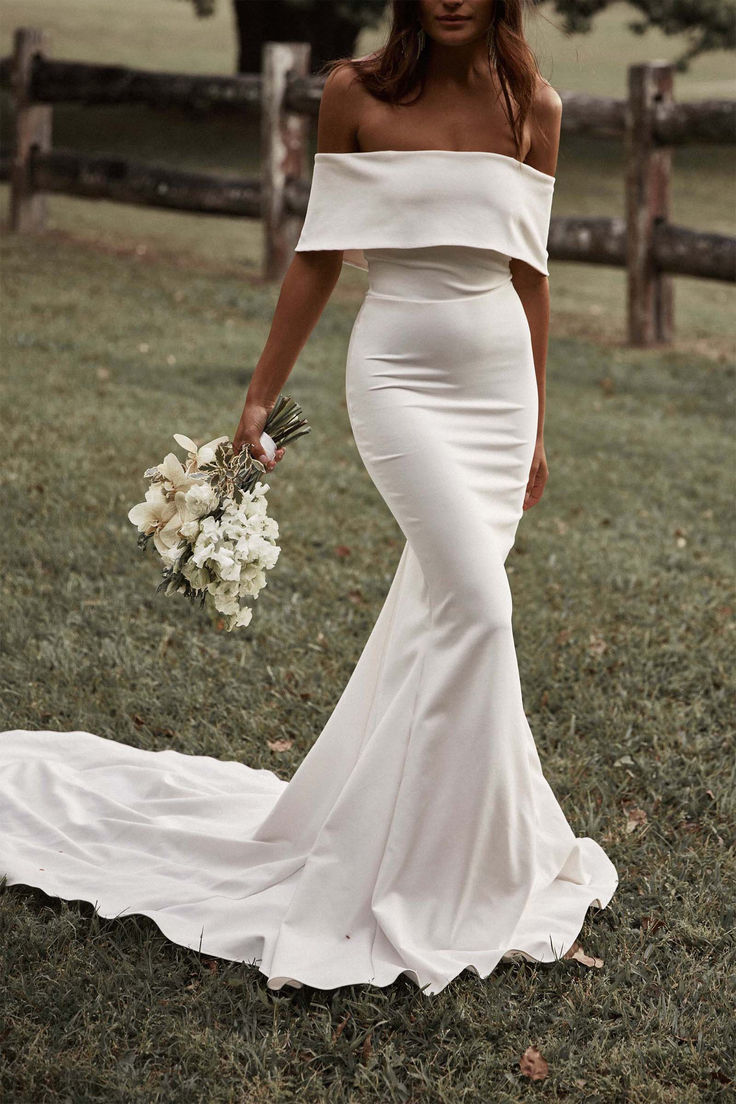 a woman in a white wedding dress holding a bouquet and posing for the camera with her hand on her hip