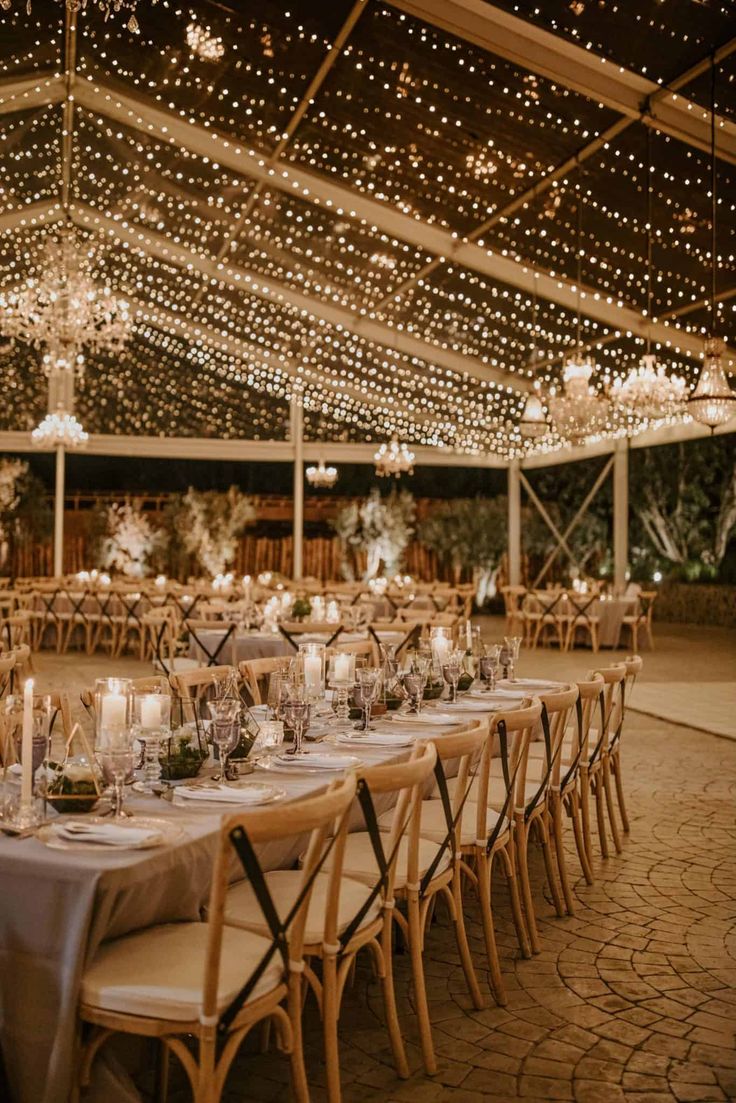 an outdoor tent with tables and chairs set up for a wedding reception at night time