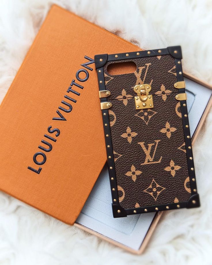 the louis vuitton phone case is next to an orange card holder on a white furnishing