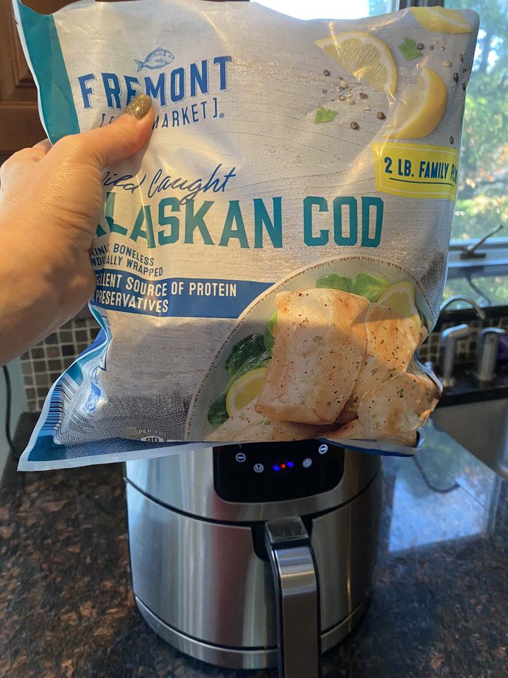 someone holding up a bag of frozen fish in front of an instant pot roaster