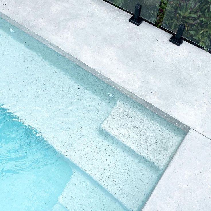 an empty swimming pool with steps leading up to the water and plants in the background