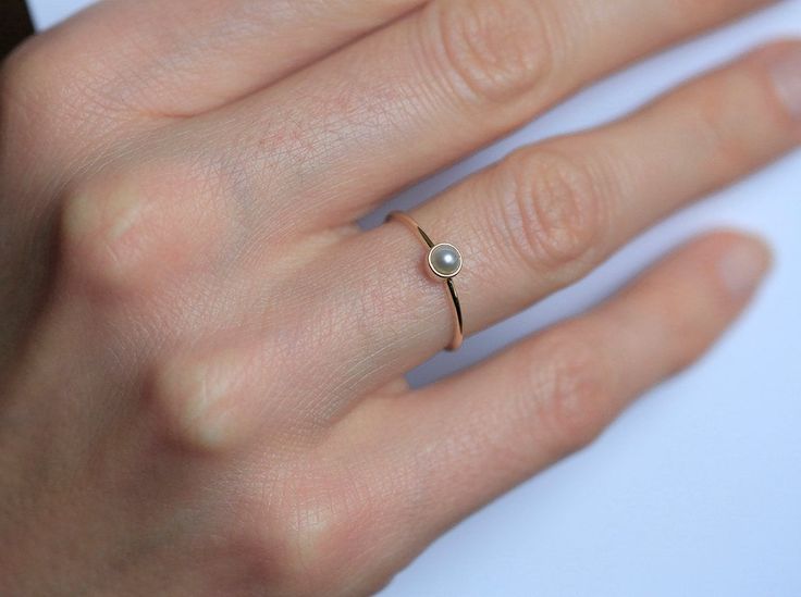 a woman's hand with a gold ring and a pearl on the middle finger