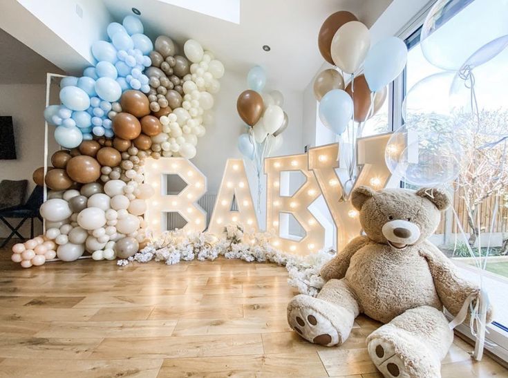 a teddy bear sitting on the floor in front of balloons and letters that spell out baby