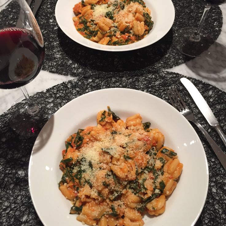 two plates of pasta with spinach and parmesan cheese next to a glass of red wine