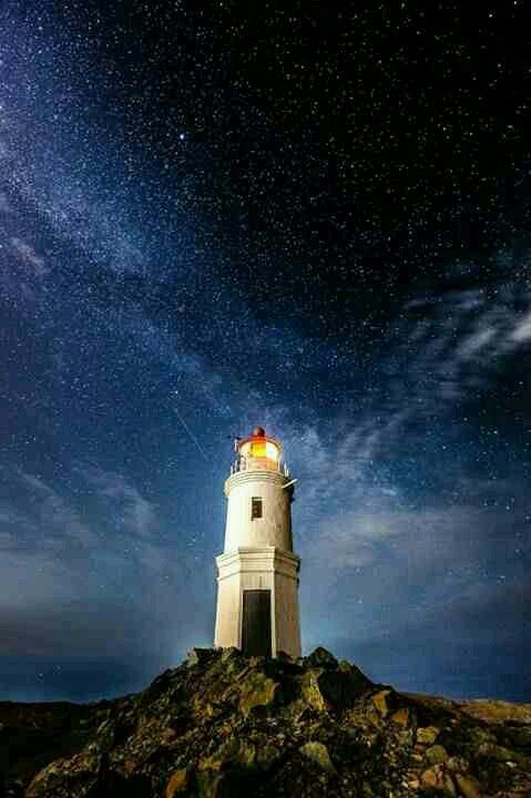 a white lighthouse sitting on top of a rocky hill under a night sky filled with stars