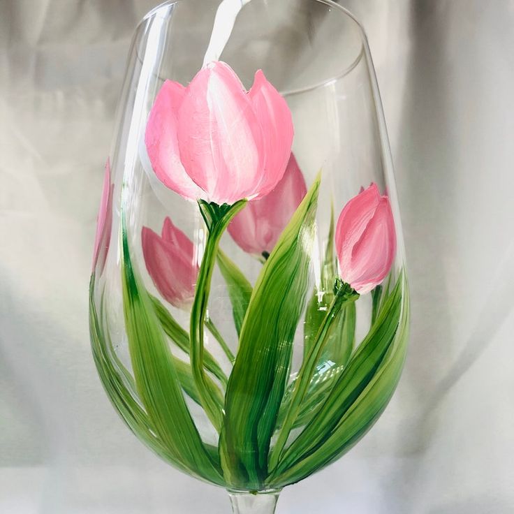 a wine glass with pink flowers painted on the inside and green leaves in the outside