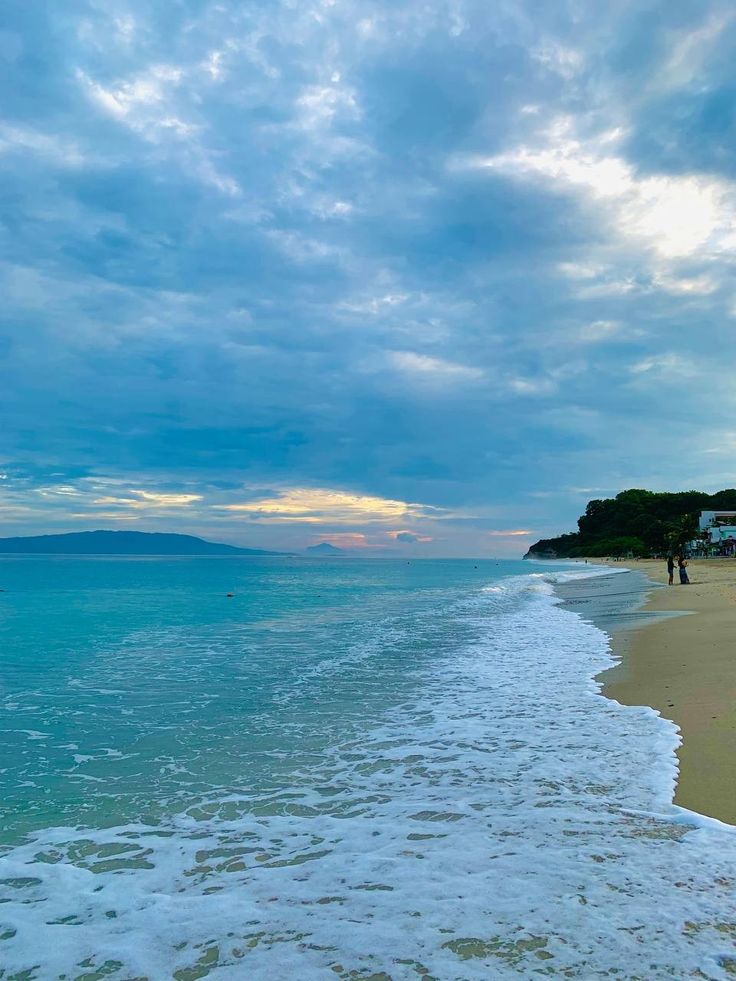 a beach with waves coming in to shore and people walking on the sand near the water