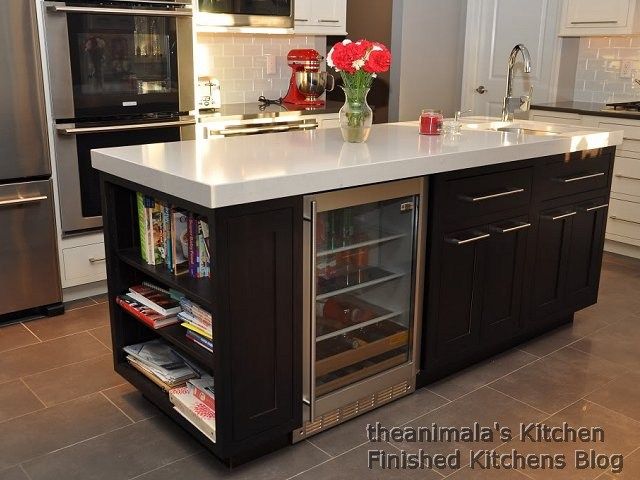 a kitchen with stainless steel appliances and white counter tops, including an island that has wine glasses on it