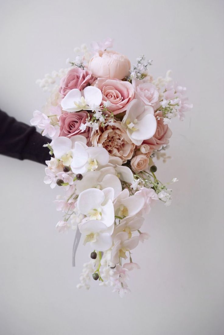 a bridal bouquet with pink roses and white orchids is held by someone's hand