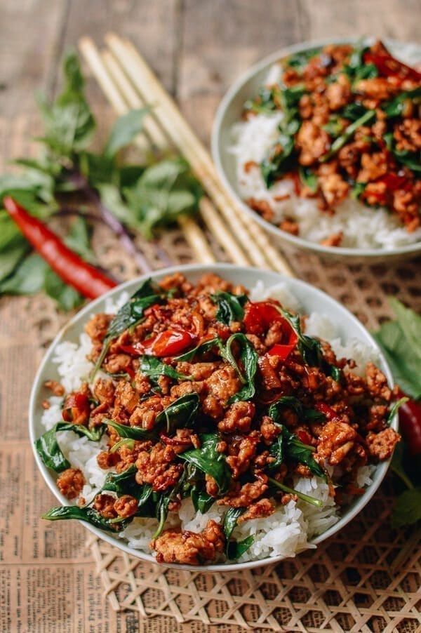 two white bowls filled with meat and vegetables on top of a woven table cloth next to chopsticks