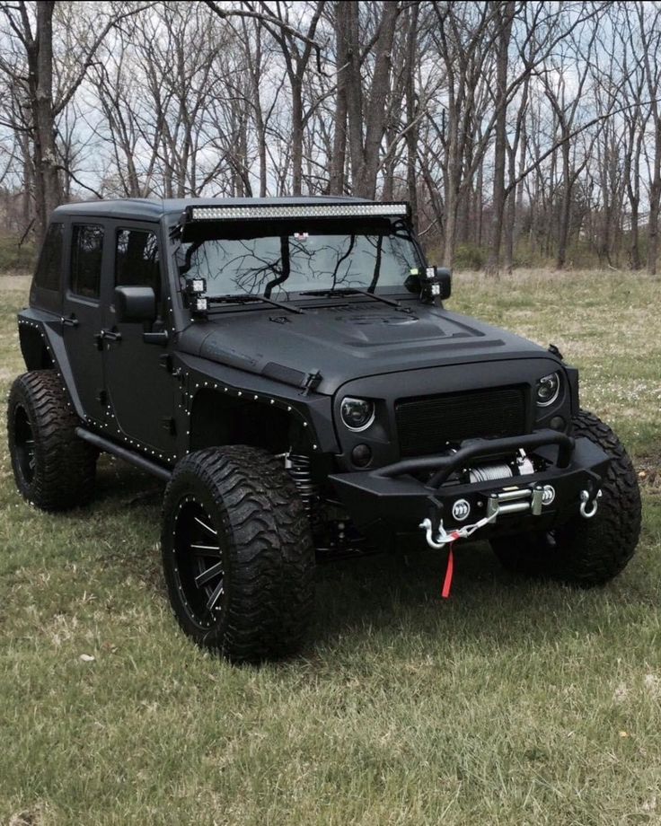 a black jeep parked in the middle of a field with trees around it and grass on both sides