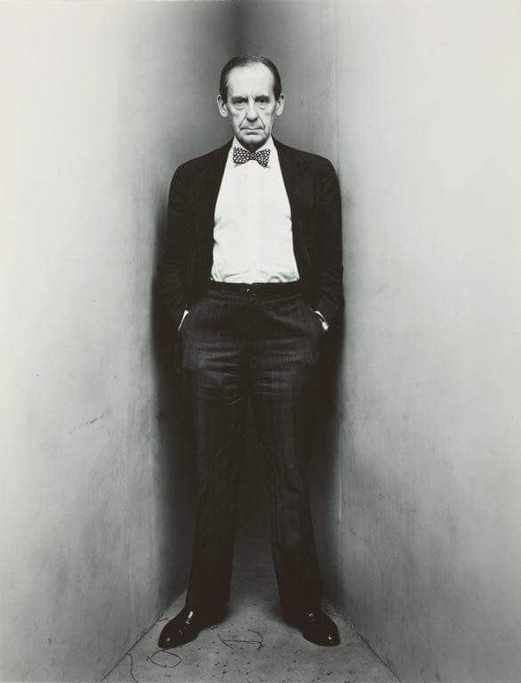 a man in a tuxedo and bow tie standing against a wall with his hands on his hips