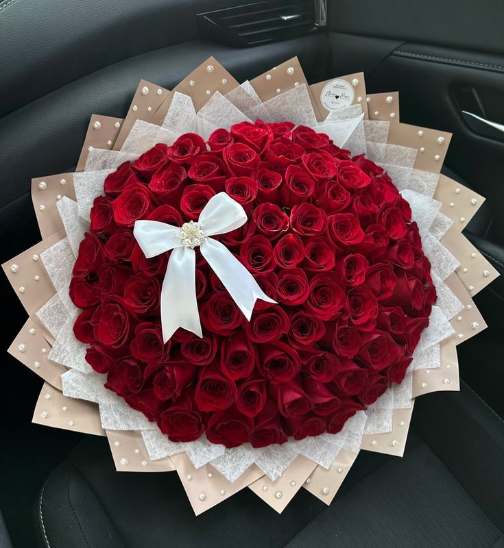 a large bouquet of red roses in the back seat of a car with a white bow