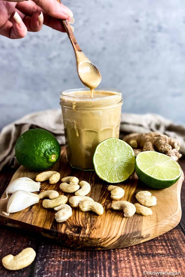 someone is dipping peanuts into a jar filled with peanut butter and limes on a wooden cutting board