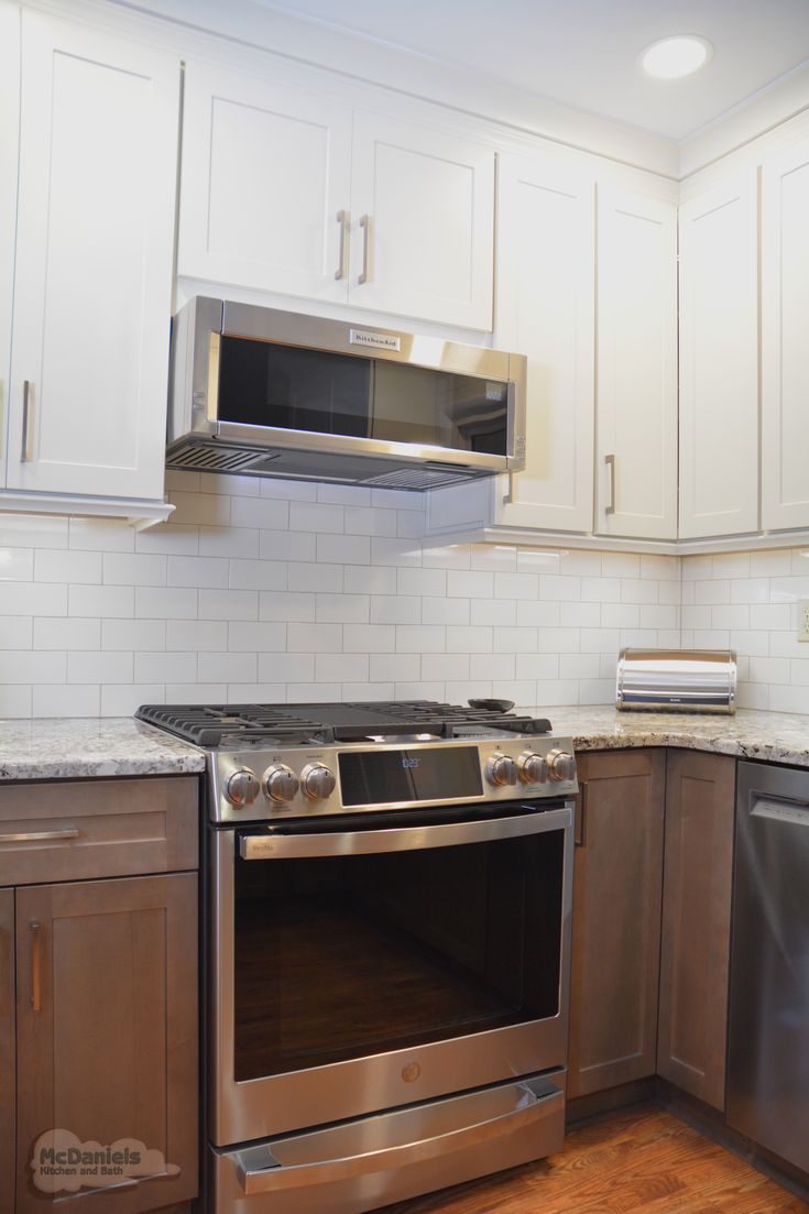 an empty kitchen with stainless steel appliances and white tile backsplash, wood flooring