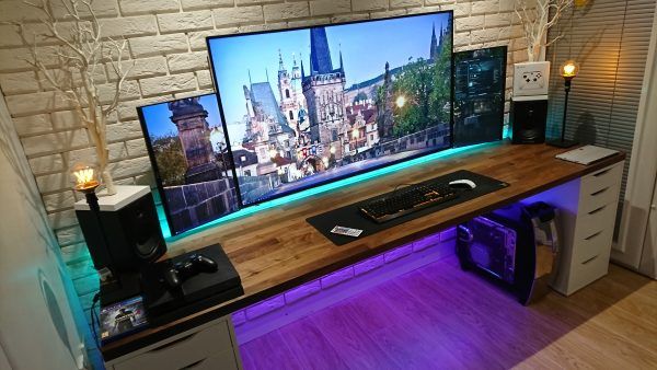 the computer desk has three monitors on it and is lit up with purple light from below