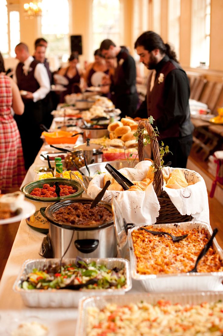 many people are standing in line to get food from the buffet table at a restaurant