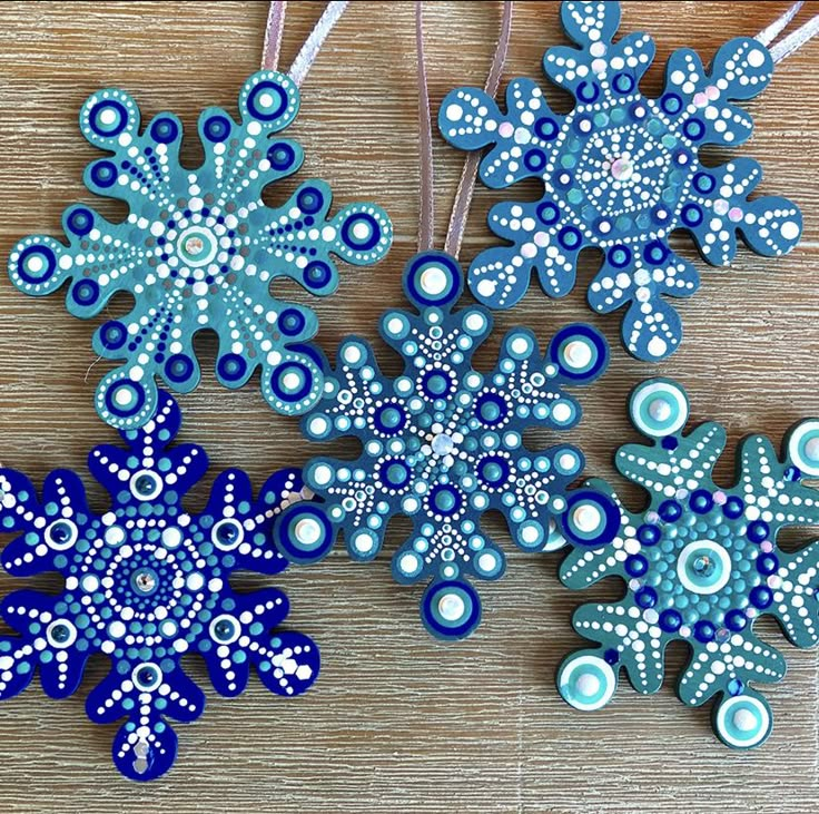 three blue and white snowflakes hanging from strings on a wooden table with beads