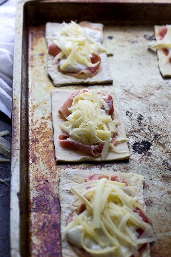 four uncooked pizzas with cheese and ham on them sitting on a baking sheet