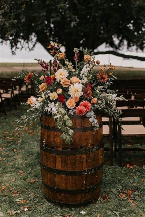 a wooden barrel with flowers and greenery on the ground in front of rows of chairs