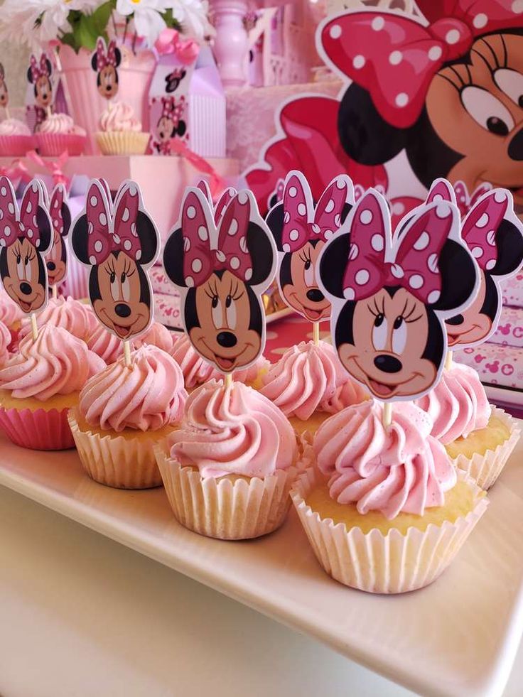 cupcakes with pink frosting and minnie mouse heads on them are sitting on a table