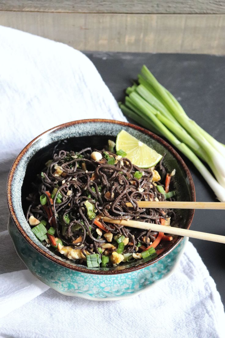 a bowl filled with noodles and vegetables on top of a white cloth next to chopsticks