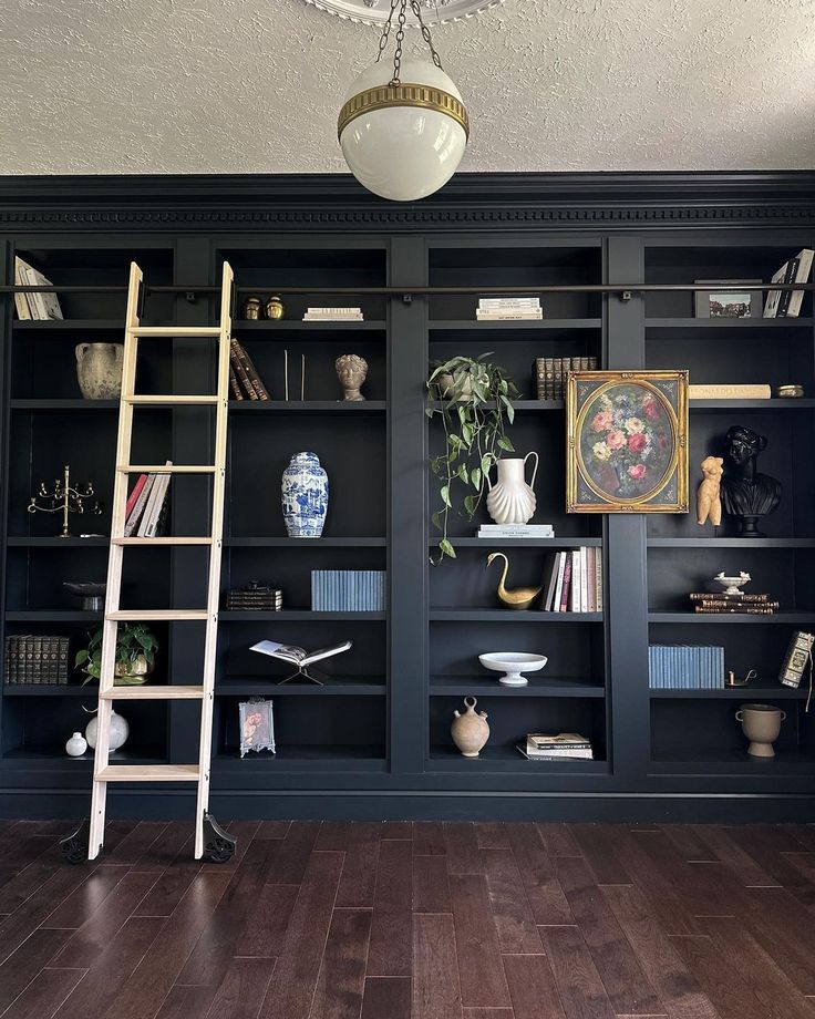 an empty room with black bookcases and wooden floors, including a ladder leaning against the bookshelf