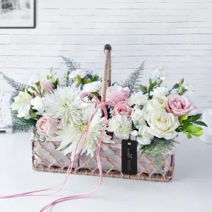 a basket filled with white and pink flowers on top of a table next to a wall