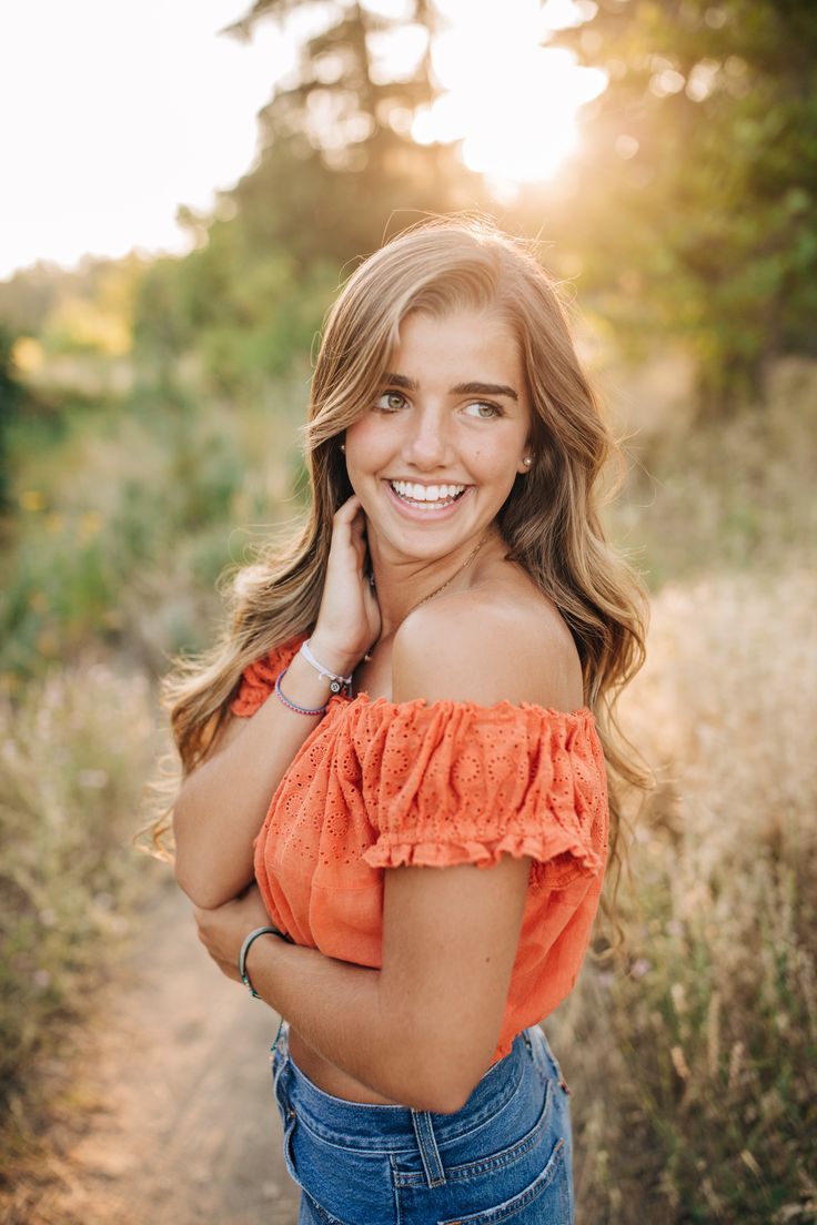 a woman in an orange top is smiling and posing for the camera with her hands on her hips