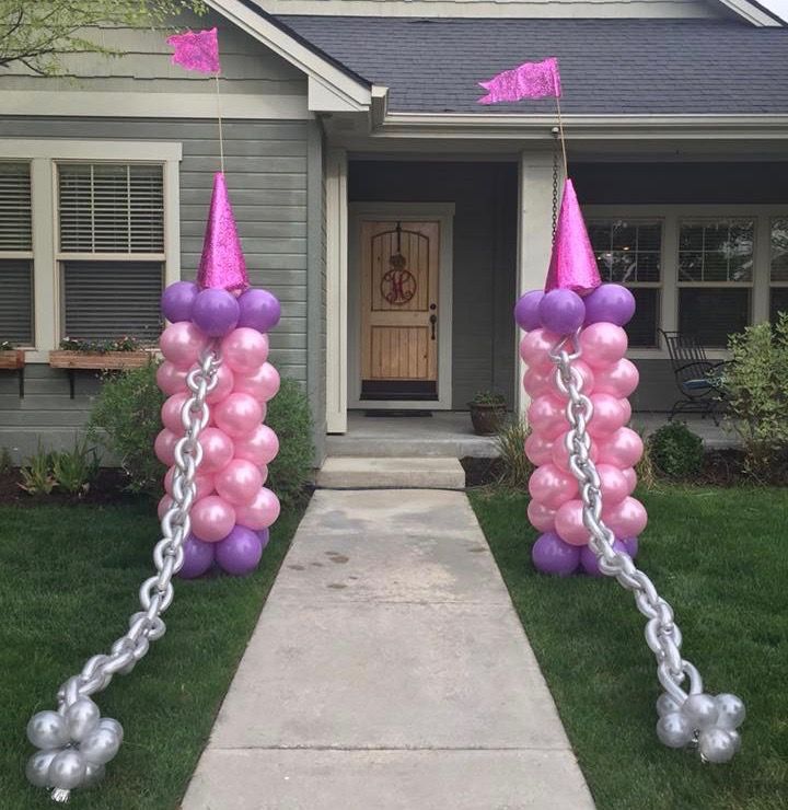 some pink and purple balloons are in front of a house with silver chains on it