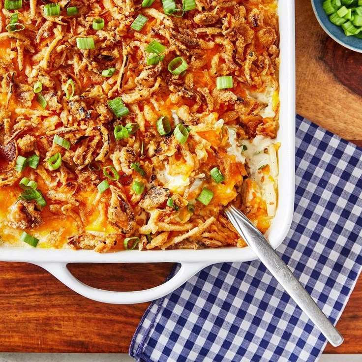 a casserole dish with meat, cheese and green onions on a wooden table