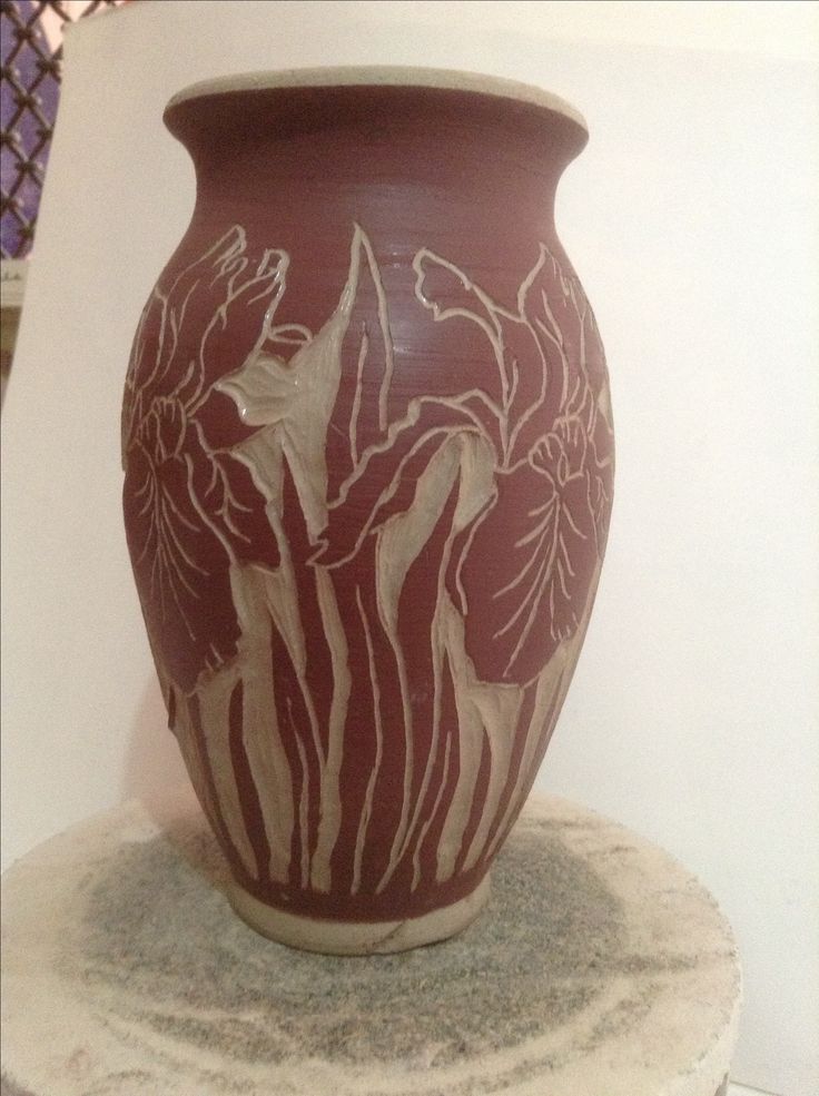 a red vase sitting on top of a white pedestal next to a wall with flowers painted on it