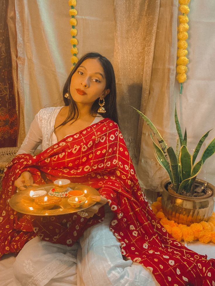 a woman sitting on a bed holding a tray with food in her hand and potted plant