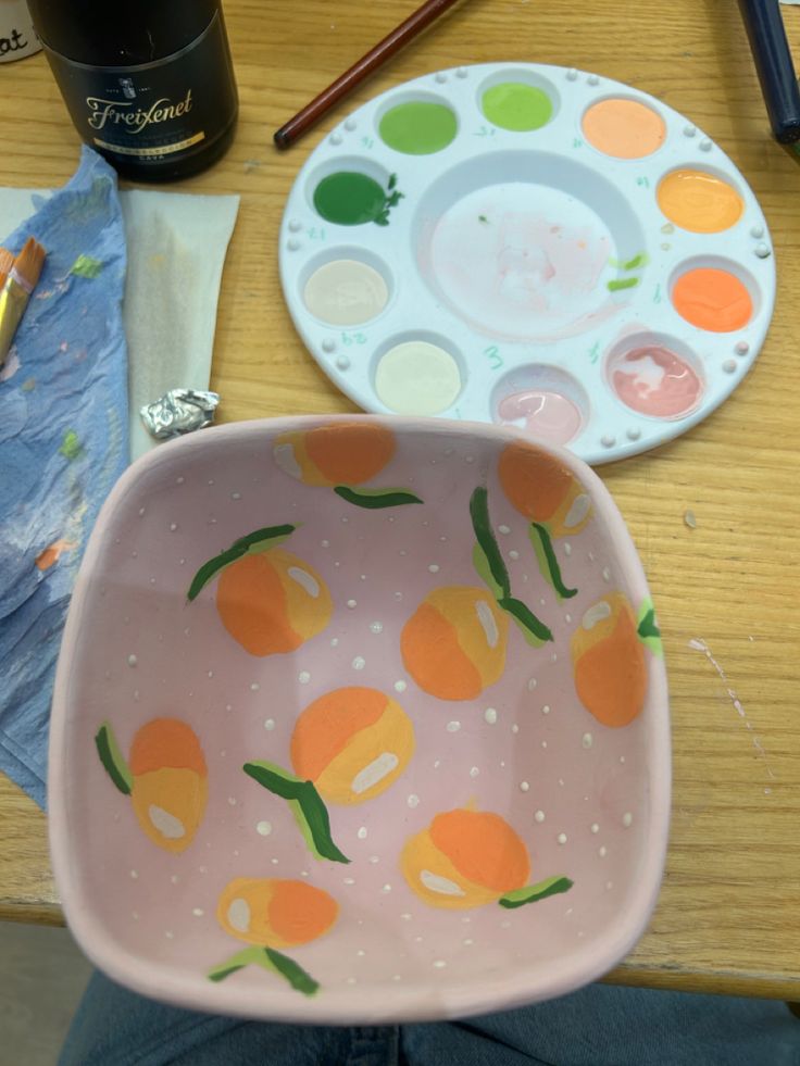 a bowl with oranges painted on it sitting next to a paintbrush and other art supplies