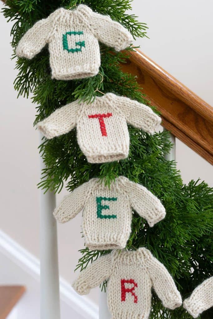 knitted sweaters hanging from the banister with letters on them and pine needles