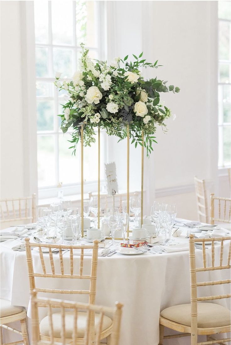 a table with white flowers and greenery in tall vases on top of it