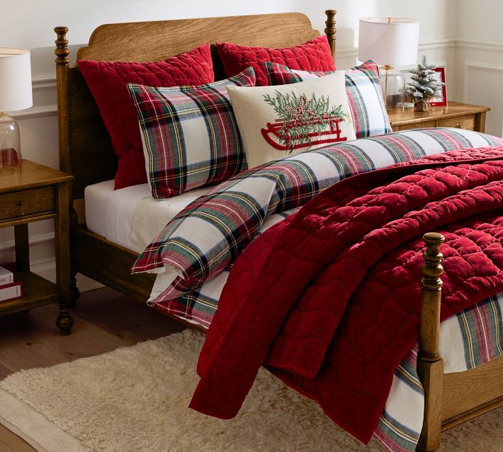 a bed with plaid comforter and pillows in a room next to a christmas tree