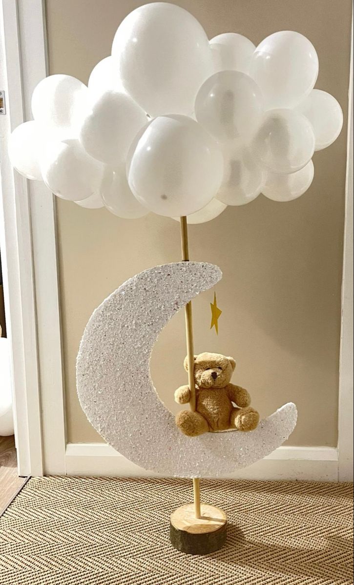 a teddy bear sitting on top of a crescent moon with white balloons in the background