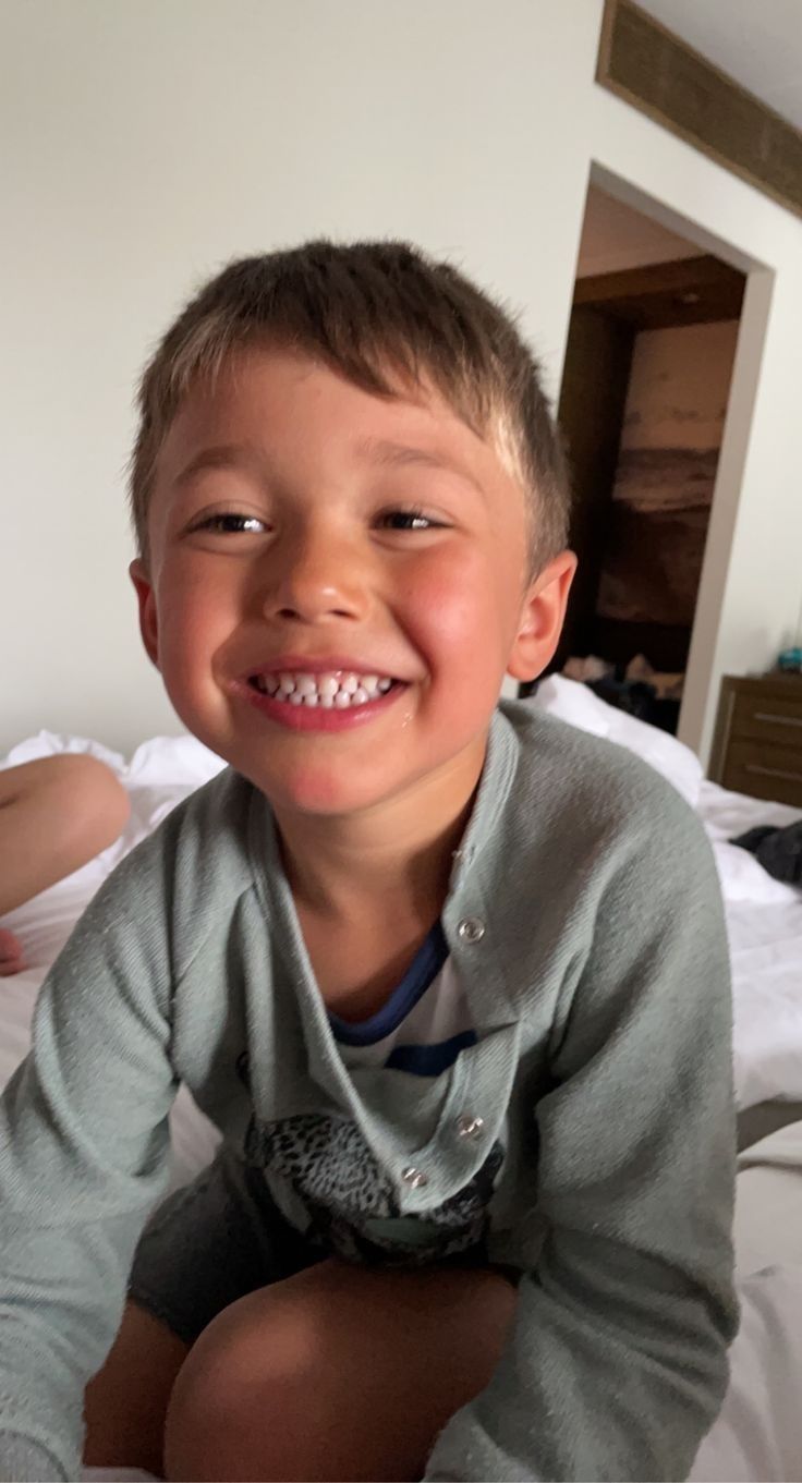 a young boy sitting on top of a bed smiling