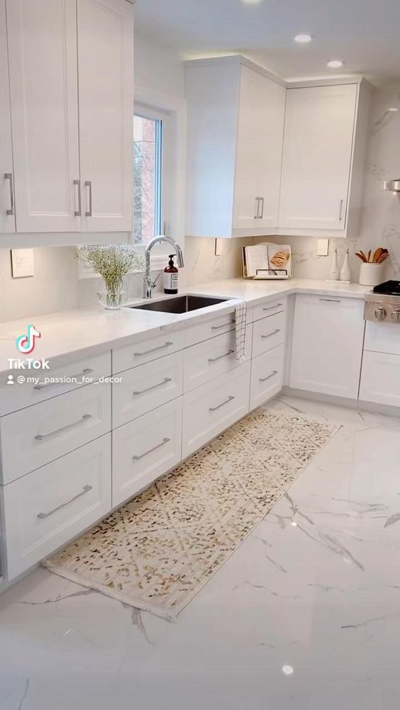 a large kitchen with white cabinets and marble flooring, including a sink and dishwasher