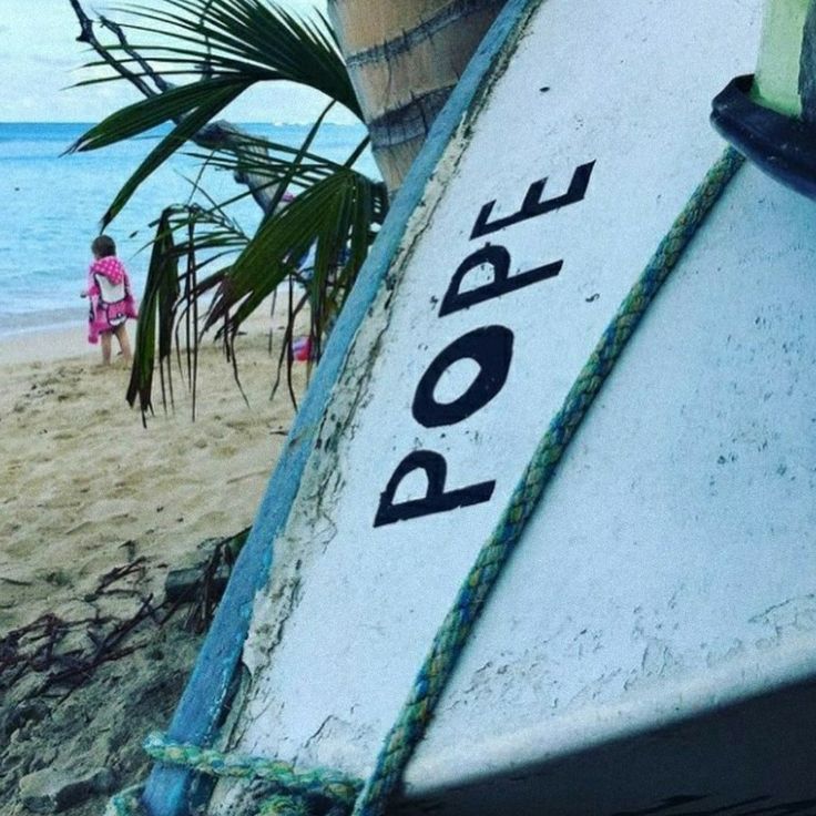 a boat sitting on top of a sandy beach next to the ocean and palm trees