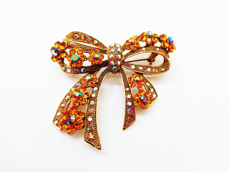 "What an elegant and glitzy splash this bow pin will make! Perfect for jazzing up any old outfit. At 2 1/2\" x 2 1/4\" it makes an impression! The pin is encrusted with many aurora borealis and gold colored stones. These faceted rhinestones catch the light and create quite a glow! Excellent condition." Glamorous Crystal Brooch As Gift, Glamorous Crystal Brooches For Gifts, Glamorous Crystal Brooches As Gift, Gold Rhinestone Pins For Party, Gold Rhinestone Party Pins, Glamorous Bling Brooches As A Gift, Glamorous Bling Brooches As Gift, Georg Jensen Silver, Old Outfits